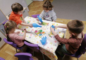 Dzieci siedzące przy stoliku i malujące talerzyki.