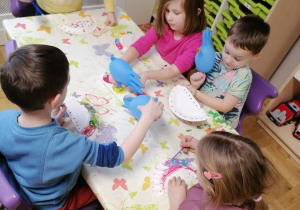 Dzieci siedzące przy stoliku i malujące talerzyki.