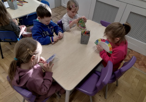 Dzieci siedzące przy stoliku i przeplatające włóczkę przez dziurki.
