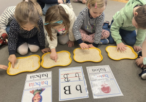 Dzieci kreślące literę B w ryżu.
