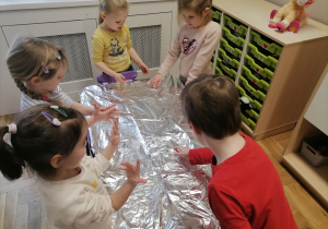 Dzieci bawiące się lodem i śniegiem na folii aluminiowej.