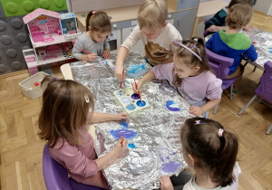 Dzieci malujące farbami po folii aluminiowej.