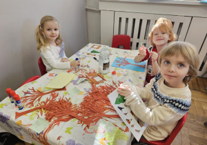 Dzieci robiące pracę plastyczną przy stoliku.