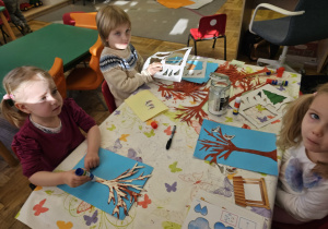 Dzieci robiące pracę plastyczną przy stoliku.