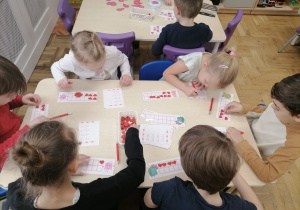 Dzieci siedzące przy stoliku i rozwiązujące zadania matematyczne.