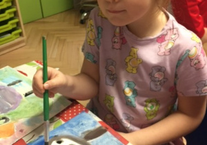 Dziewczynka malująca dinozaura farbami.