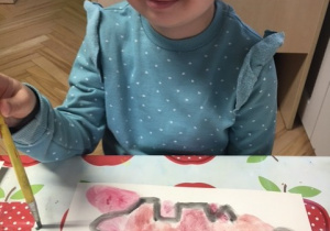 Dziewczynka malująca dinozaura farbami.
