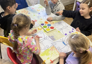 Dzieci siedzące przy stoliku i malujące motyle.