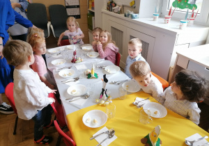 Dzieci w eleganckich strojach siedzące przy wielkanocnym stole.