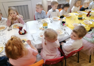 Dzieci w eleganckich strojach siedzące przy wielkanocnym stole.