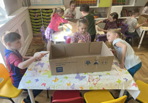 Dzieci siedzące przy stoliku i malujące pudełko farbami.