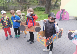 Dzieci w ogrodzie przedszkolnym w wykonanych przez siebie kartonowych autach.