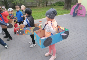 Dzieci w ogrodzie przedszkolnym w wykonanych przez siebie kartonowych autach.