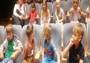 Dzieci siedzą w dwóch rzędach na fotelach kinowych