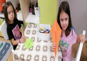 Dwie dziewczynki składają latwce z kolorowego papieru