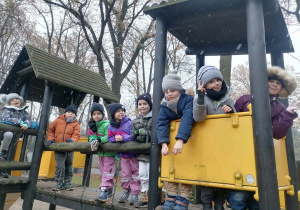 Dzieci pozują do zdjęcia stojąc na drewnianym zestawie ogrodowym