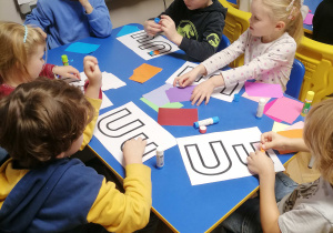 Dzieci przy stoliku wyklejają kolorowym papierem kontury litery U