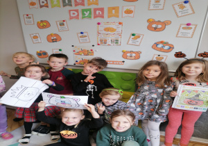 Dzieci pozują do zdjęcia z kolorowankai na tle dekoracji z okazji Dnia dyni