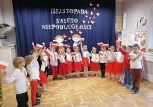 Dzieci w strojach biało czerwonych machają flagami podczas uroczystości