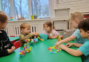 Dzieci siedzą przy stoliku i układają klocki