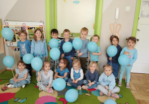 Dzieci ubrane na niebiesko pozują do zdjęcia z niebieskimi balonami