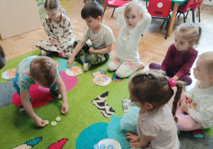 Dzieci siedzą na dywanie i przeliczają papierowe jajka