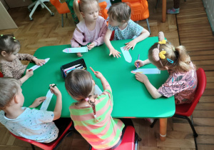 Dzieci siedzą przy stoliku i wykonują zakładkę do książki