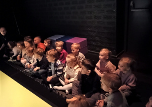 Dzieci siedzą a poduszkach i oglądają przedstawienie teatralne