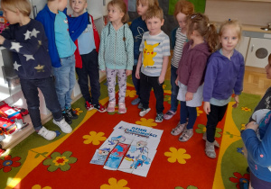 Dzieci stoja w kole, w środku znajduje się ułożony plakat pokolorowany przez dzieci.