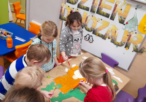Grupa dzieci maluje farbami fotobudkę z dinozaurami