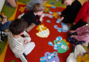 Dzieci układają na kolorowych parasolkach obrazki z przedmiotami na daną literę.