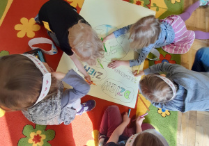 Dzieci na dywanie kolorują plakat z okazji Dnia Ziemi.