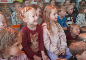 Na pierwszym planie znajduja się trzy usmiechnięte dziewczynki które oglądają przedstawienie teatralne, w tle widać resztę dzieci.