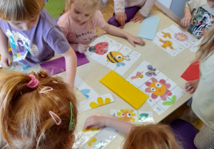 Grupa dzieci siedzi przy stoliku i uklada wiosenne puzzle.