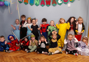 Dzieci w strojach karnawałowych pozują do zdjęcia na tle napisu Bal karnawałowy.