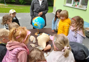 Dzieci oglądają globus oraz muszle, specjalista tlumaczy dzieciom gdzie występuje rafa koralowa oraz co to dokładnie oznacza.